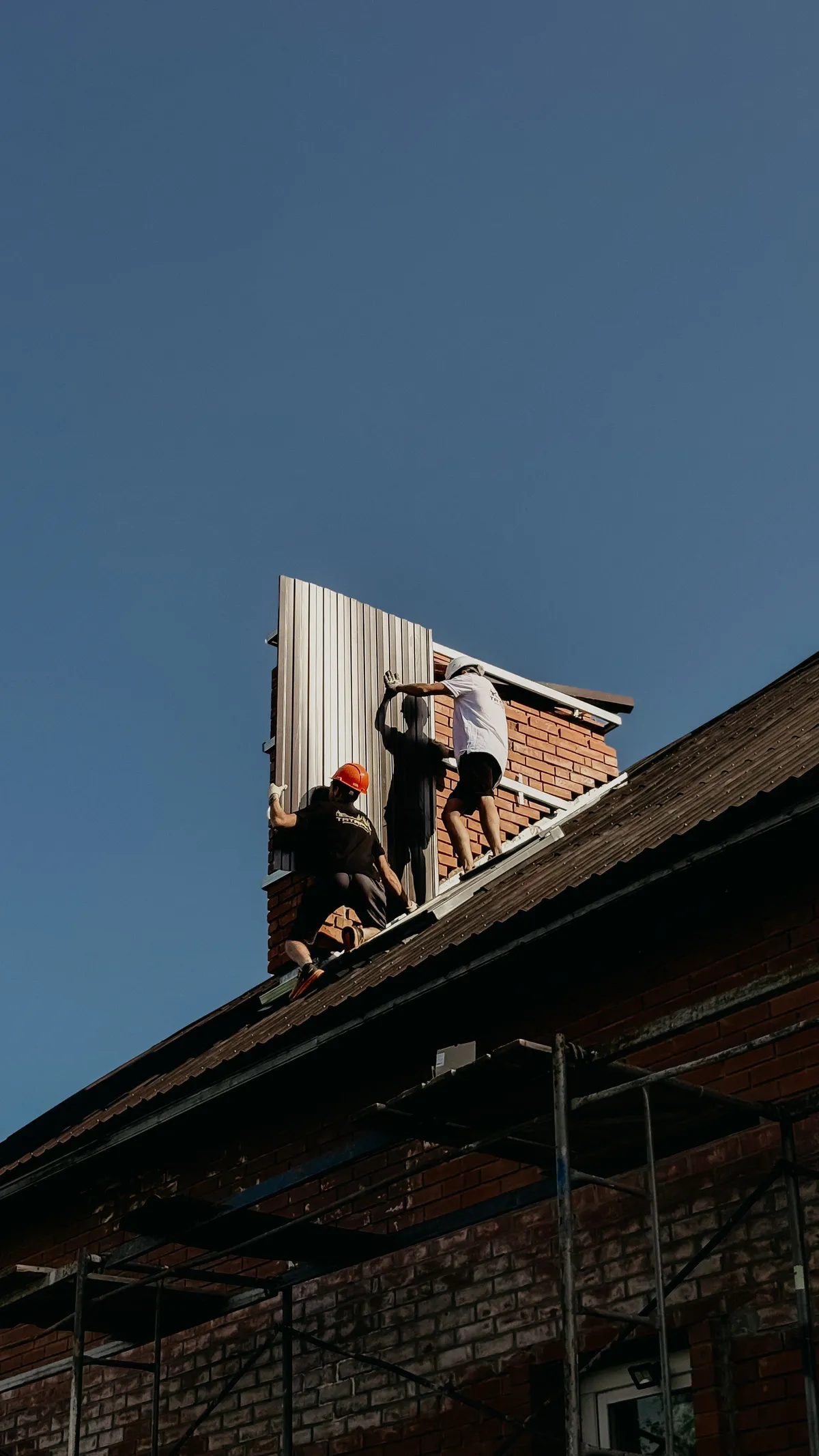 Two roofers installing metal panels on a gable