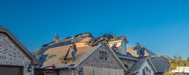 Roofing crew tearing off and replacing shingles on a brick home, work truck parked in the driveway
