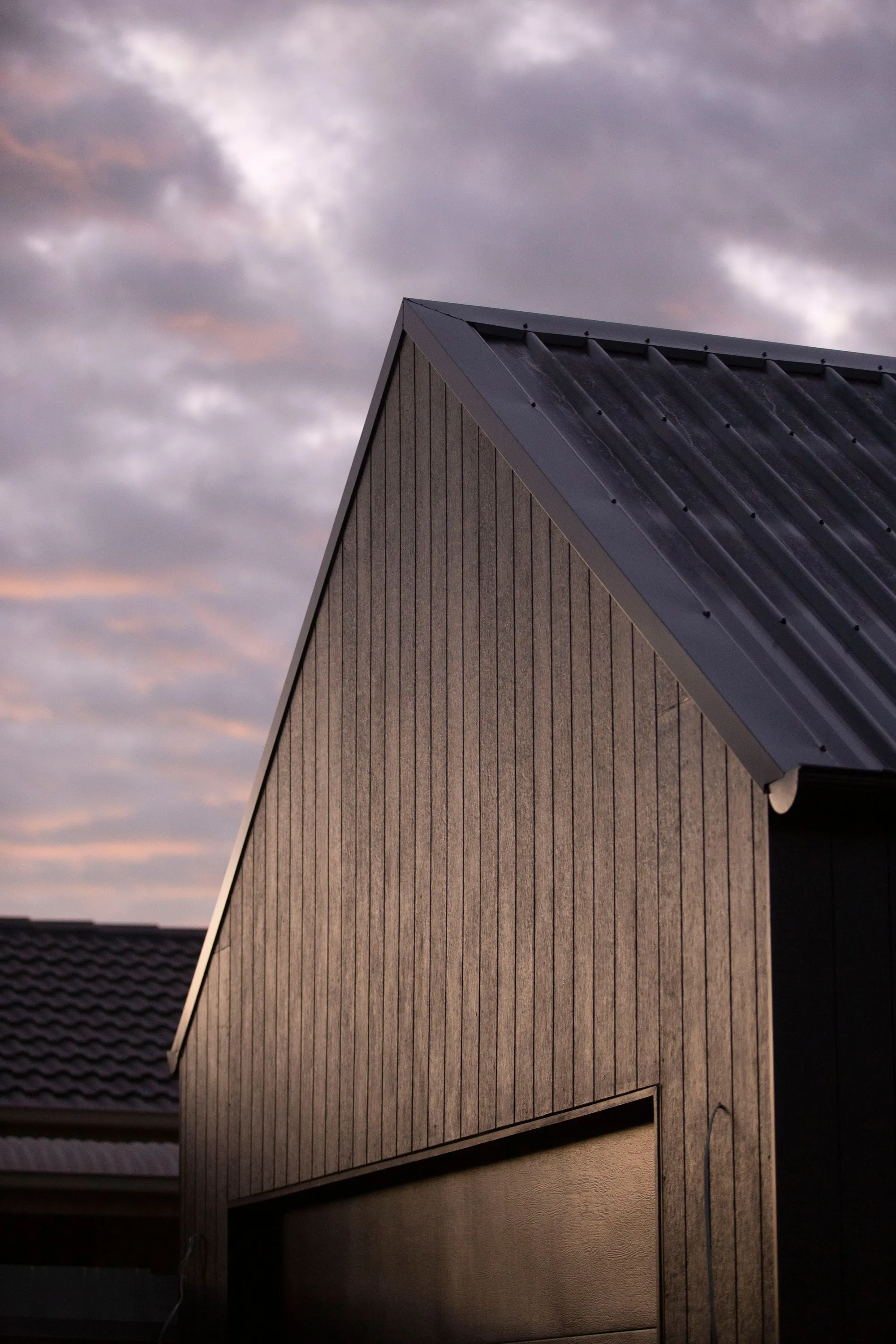 Dark standing-seam metal roof gable at dusk with warm sky