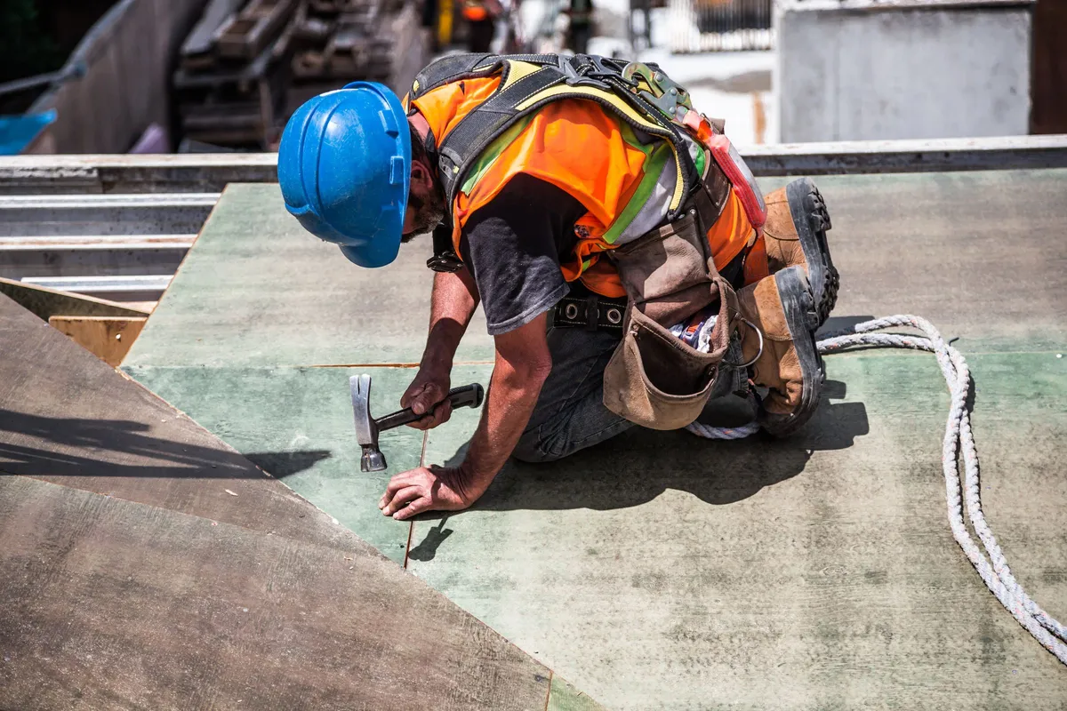 Roofer in safety harness installing roof sheathing
